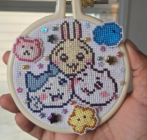 Chiikawa Cross Stitch A cross stitch of Chiikawa, Usagi and Hachiware. There are small cross stitches of their pochettes (Teddybear, star and fish) surrounding them. There are also beads sewn into the fabric.